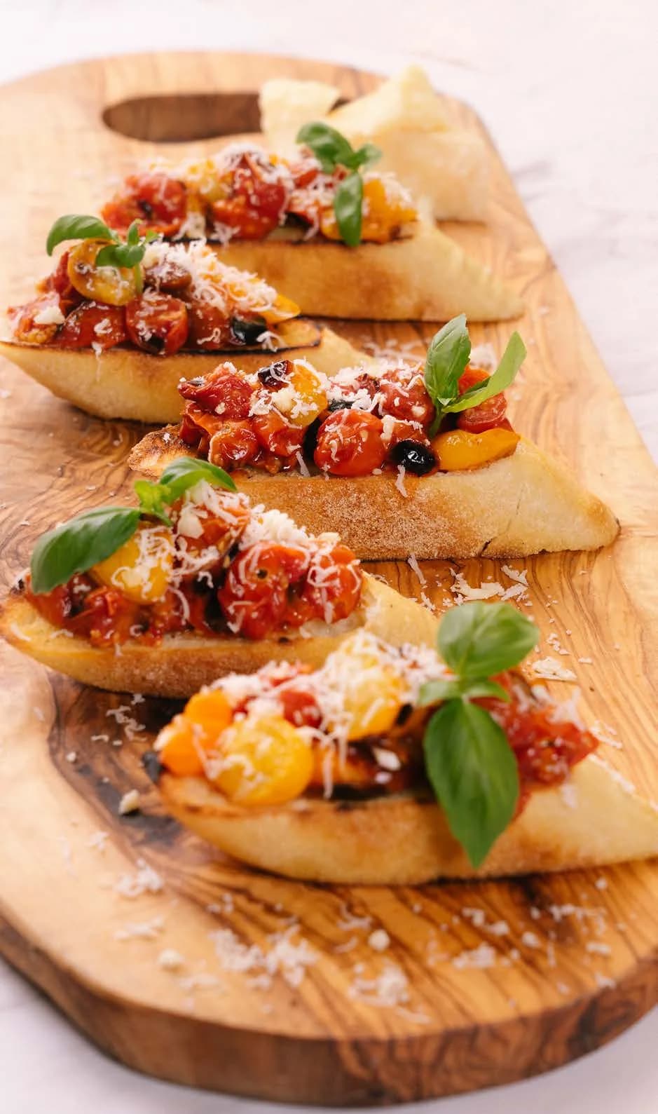 Blistered cherry tomato bruschetta with basil and grated cheese on a wooden board