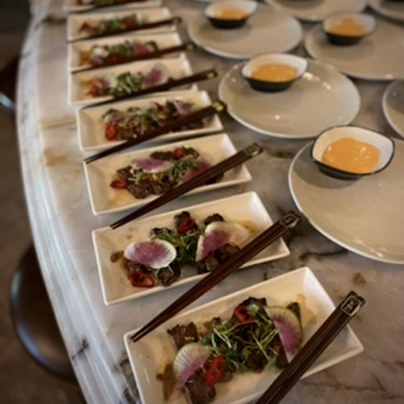 A row of Chef Lauren Lawless's beef small plates with watermelon radish, microgreens and chopsticks