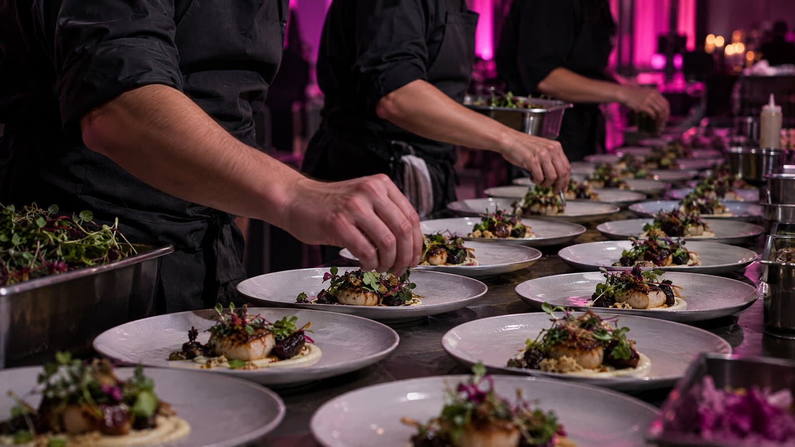 A catering team plating rows of dishes on site